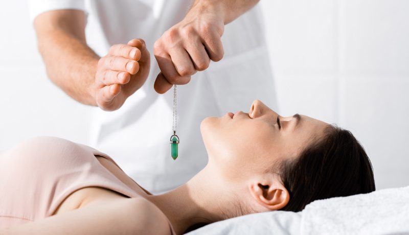 cropped view of hypnotist standing near woman on pillow and holding green stone